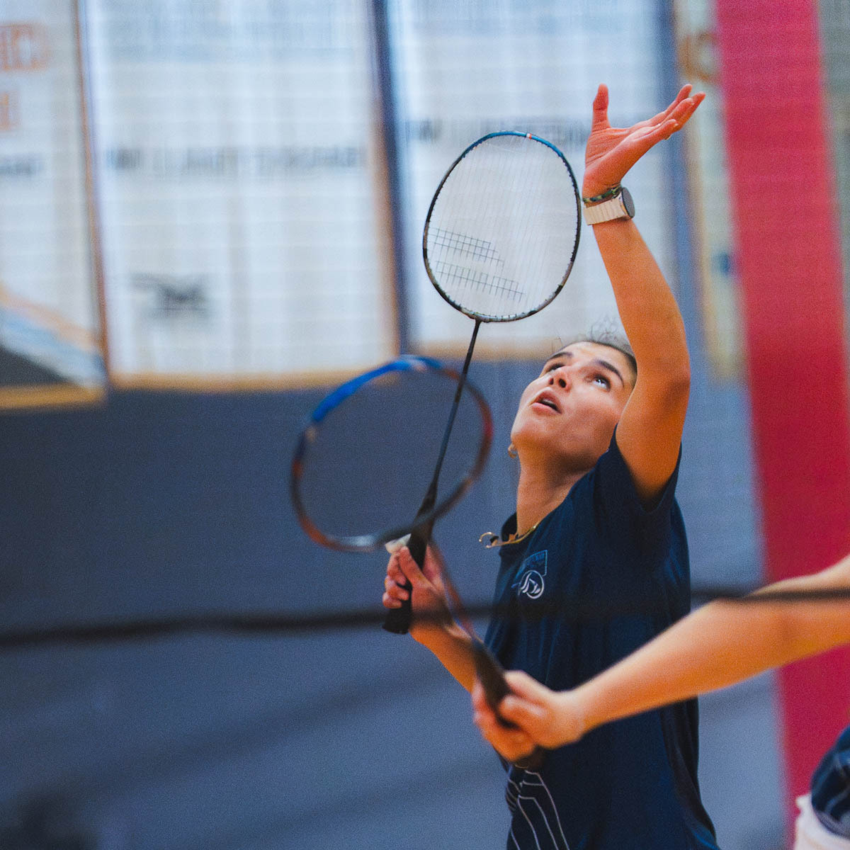 Une joueuse de badminton se prépare à frapper le volant, concentrée sur le jeu dans une salle de sport animée.