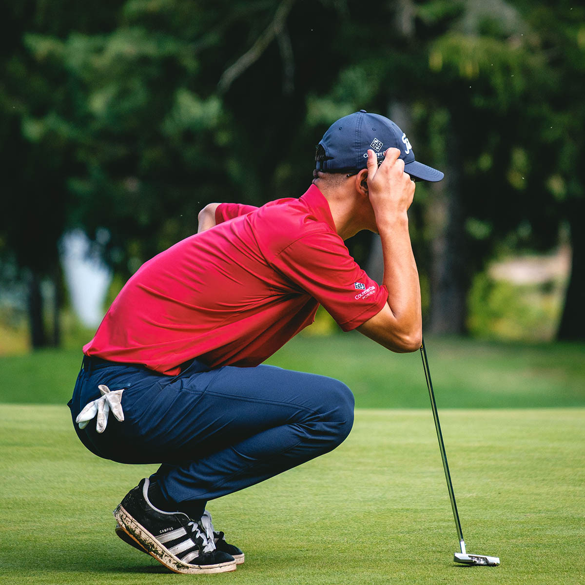 Un golfeur s'accroupit, concentré sur son coup, prêt à réaliser un putt sur un green ensoleillé.