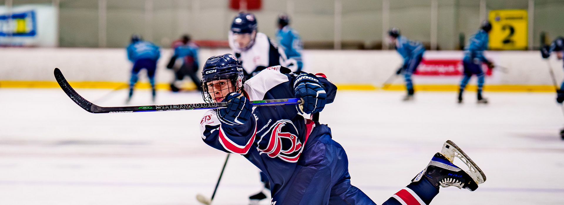 A focused hockey player skates with determination, aiming to make a shot amidst teammates and opponents on the ice.