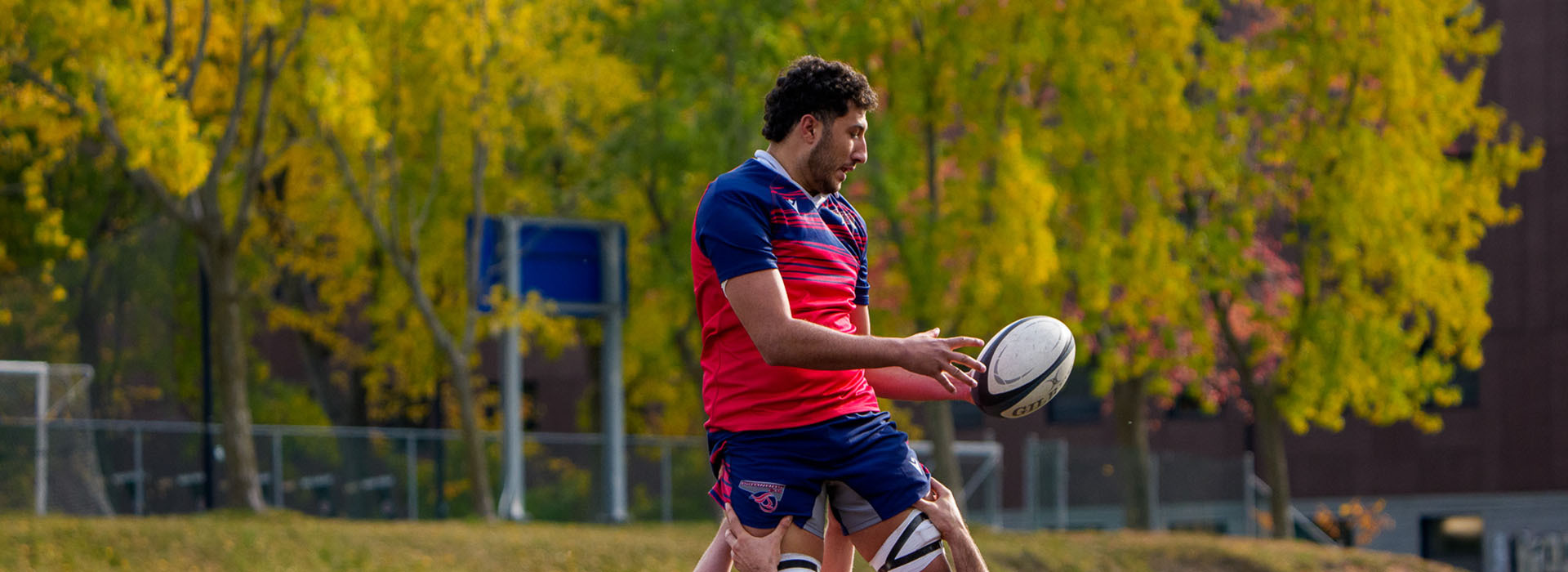 Un joueur de rugby s'apprête à effectuer une passe sous un ciel automnal, entouré de couleurs vives des feuillages.