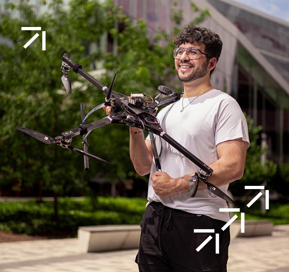 Étudiant souriant tenant un drone sur le campus.