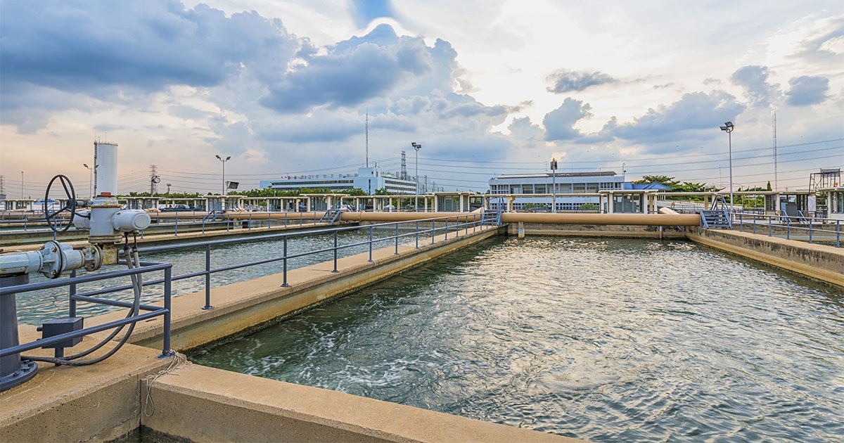 Vue d'une station de traitement des eaux, avec plusieurs bassins et infrastructures modernes sous un ciel nuageux.