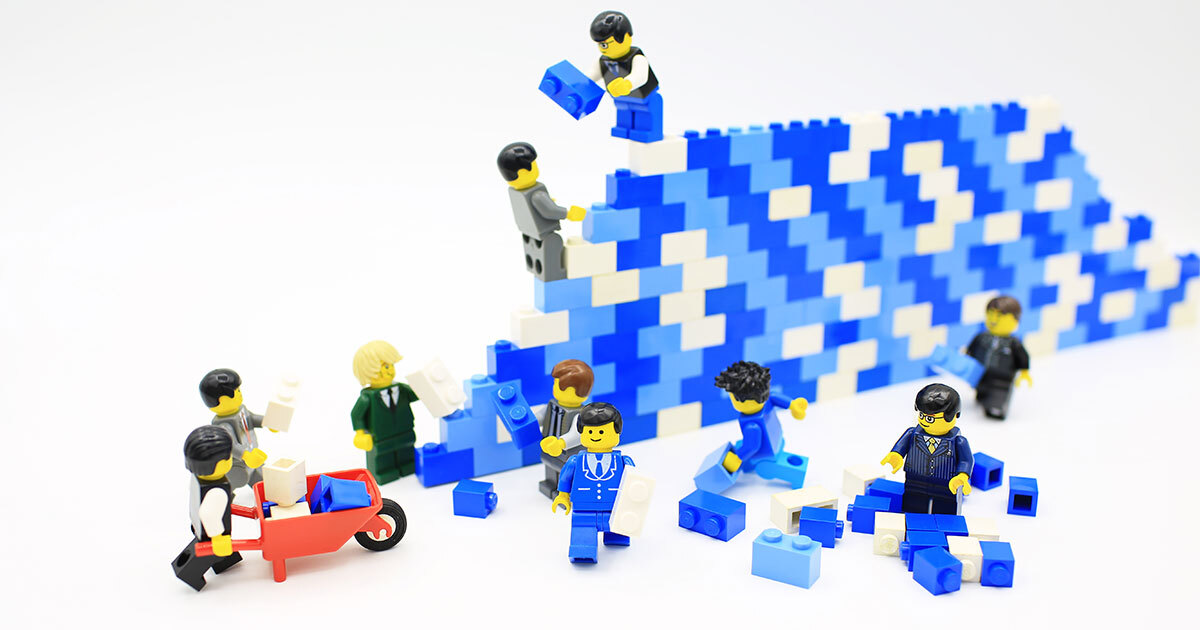 Des personnages en Lego travaillent ensemble à construire un mur coloré, illustrant la coopération et l'innovation.