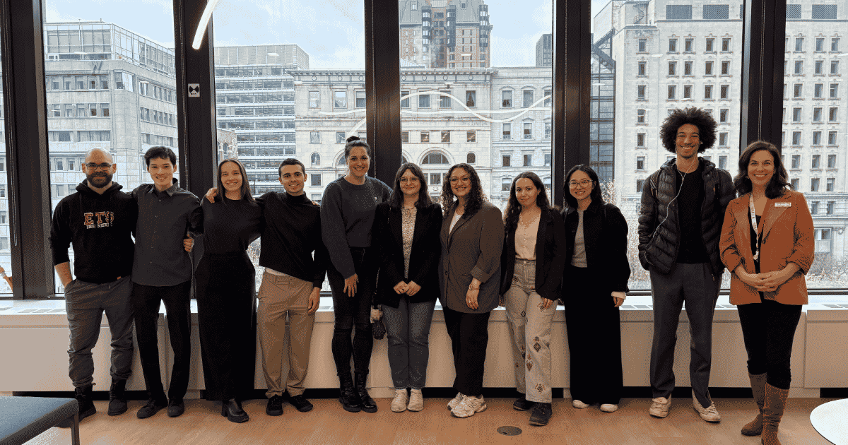 Un groupe d'étudiants et de professeurs souriants se tient près d'une grande fenêtre, avec une vue sur des bâtiments urbains en arrière-plan.