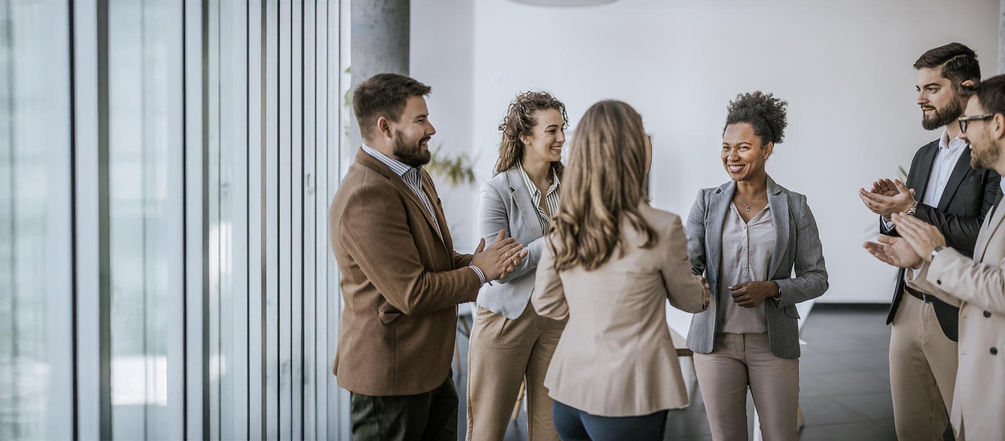 A diverse group of professionals engaged in a warm handshake, celebrating achievements in a modern office setting.