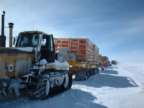 Convoy de tracteurs sur neige, transportant du matériel.