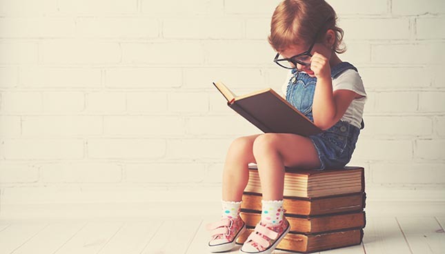 Enfant studieux lisant posé sur pile de livres.