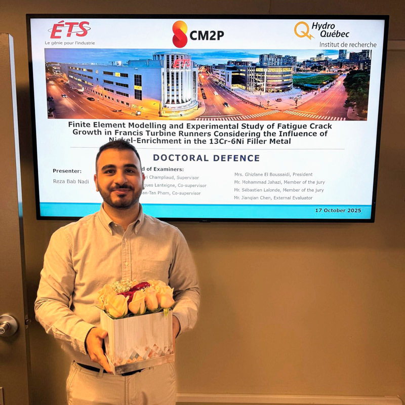 Un candidat souriant présente sa soutenance de doctorat entouré de fleurs, mettant en avant son travail de recherche en ingénierie.