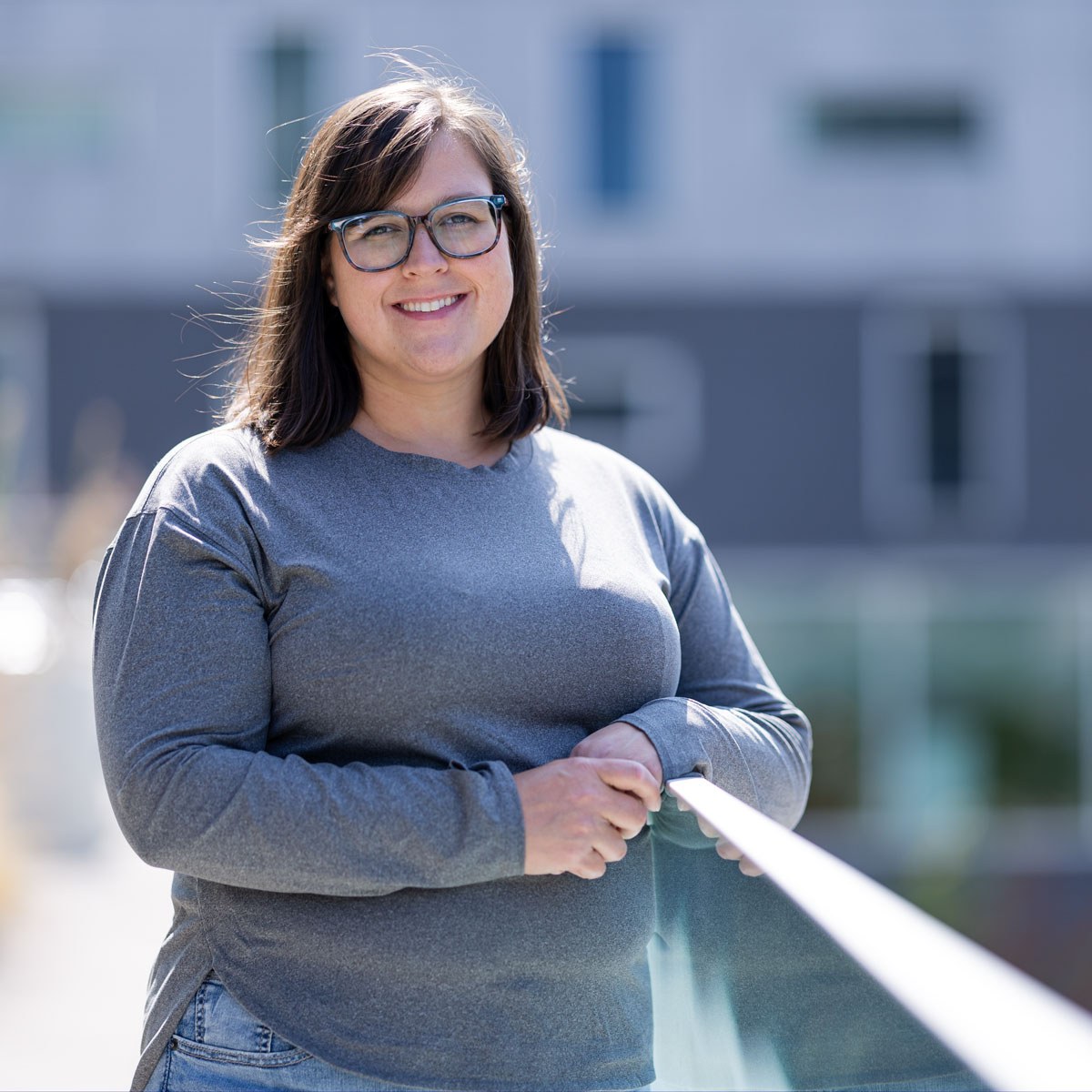 Souriante, une étudiante se tient près d'une rambarde, dans un cadre moderne, témoignant de la vie dynamique du campus.