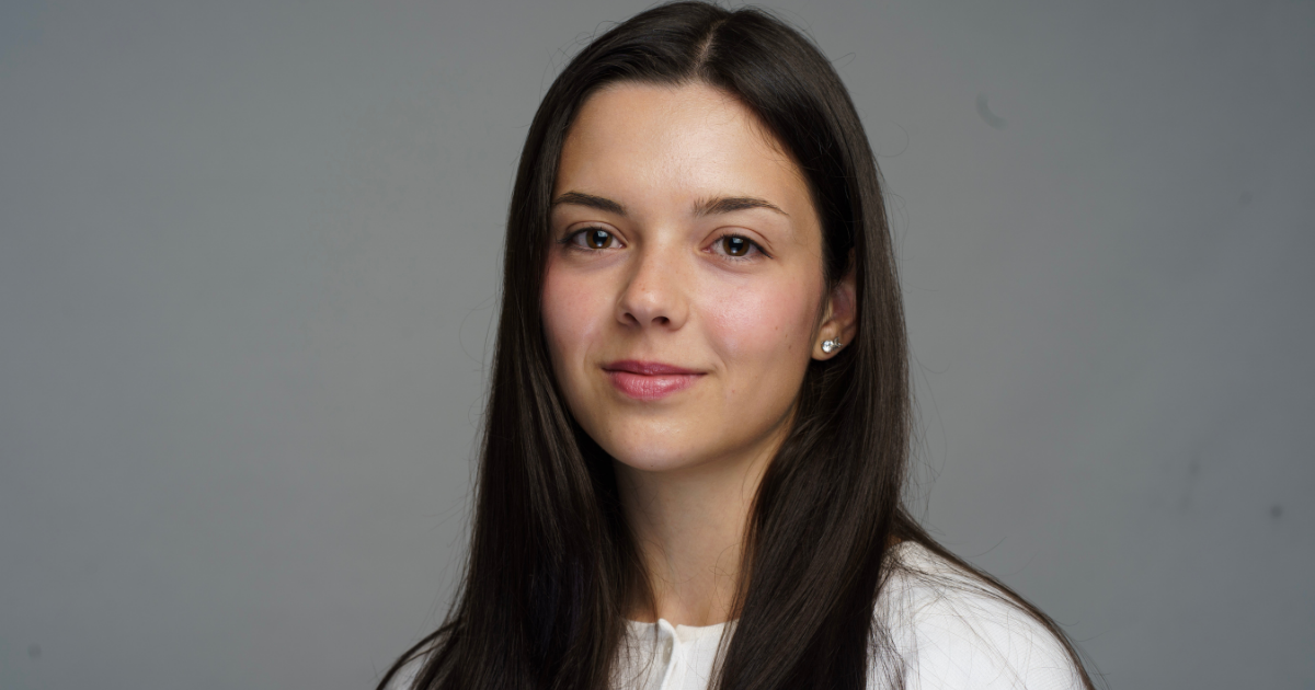 Portrait d'une jeune femme, souriante, avec de longs cheveux bruns et une tenue claire, dégageant confiance et détermination.