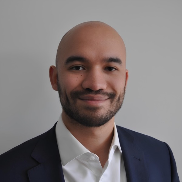 Jeune professionnel souriant, vêtu d'un costume sombre, il dégage une image de confiance et de détermination.