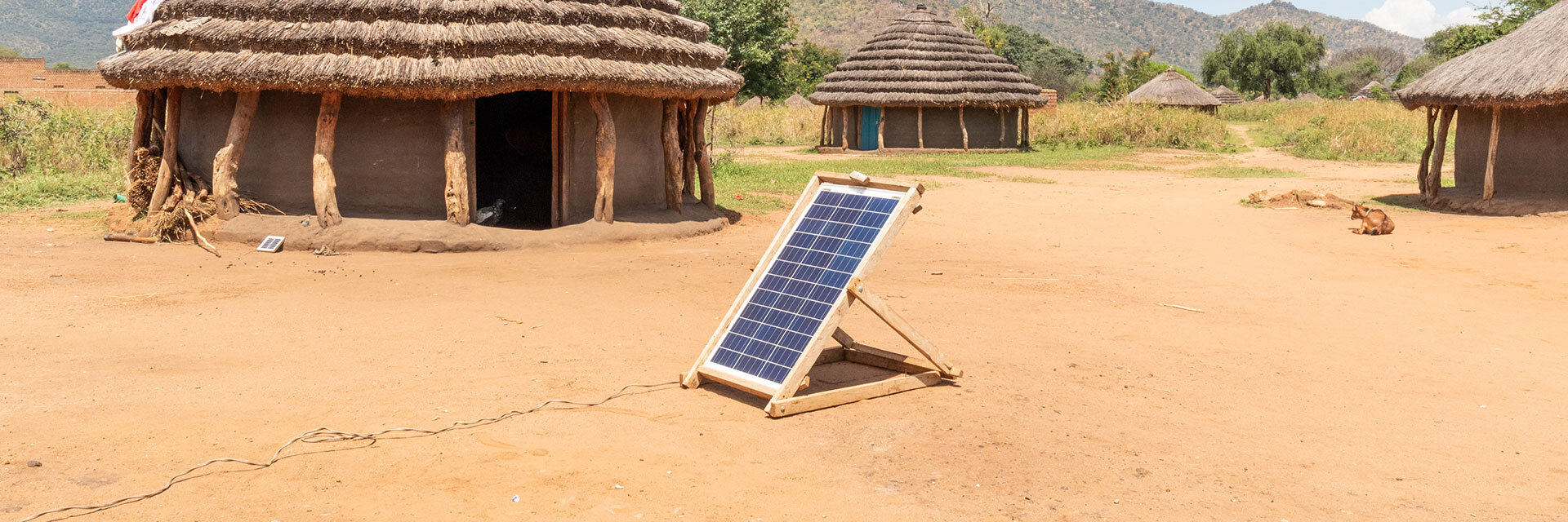 Panneau solaire devant des huttes traditionnelles, énergie propre en milieu rural.