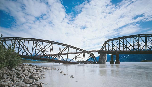 Pont en treillis métallique sur rivière, ingénierie et nature cohabitent.