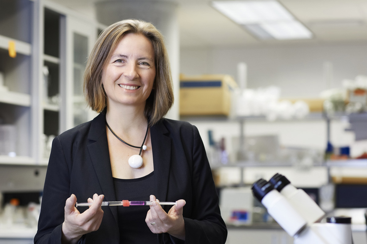 La professeure-chercheuse Sophie Lerouge, souriante dans un laboratoire en technologies de la santé affilié à l'ÉTS, tenant un tube à essai, entourée d'équipements scientifiques modernes.