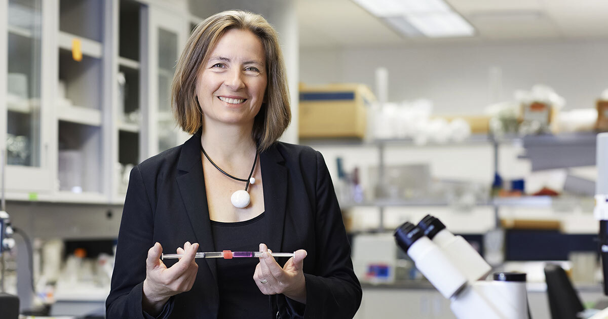 Une chercheuse souriante présente un échantillon dans un laboratoire moderne, mettant en avant l'innovation scientifique.