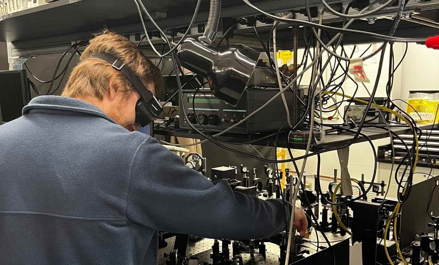 Un étudiant manipule des équipements complexes dans un laboratoire de recherche technologique, entouré de câbles et d'instruments scientifiques.