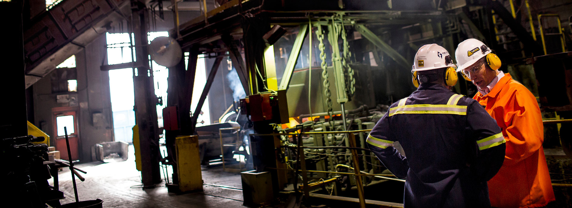 Deux professionnels discutent dans un environnement industriel, sous une lumière tamisée, au cœur d'une installation technologique.
