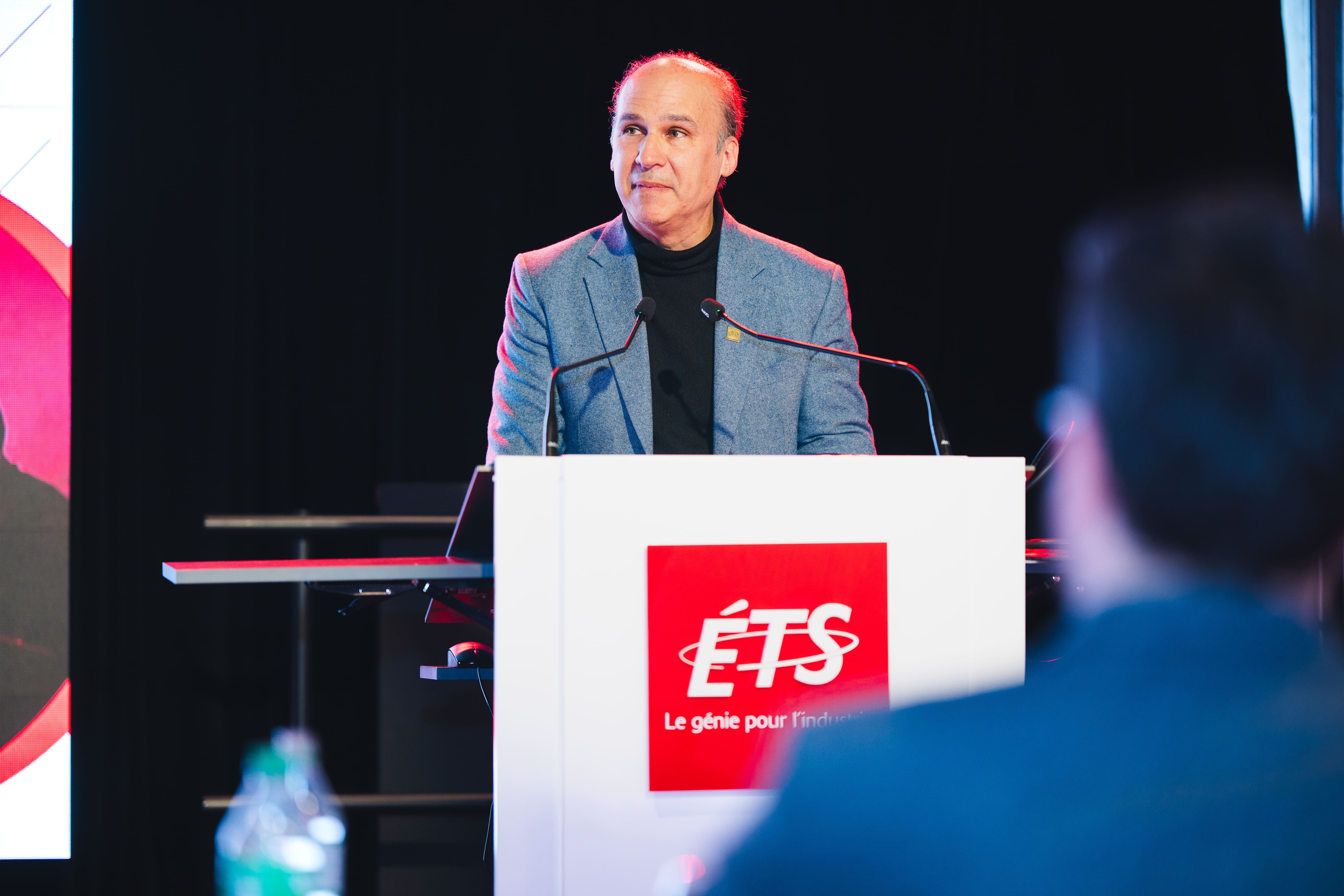 Un intervenant s'adresse à un public lors d'un événement à l'ETS, promouvant l'innovation et le génie.
