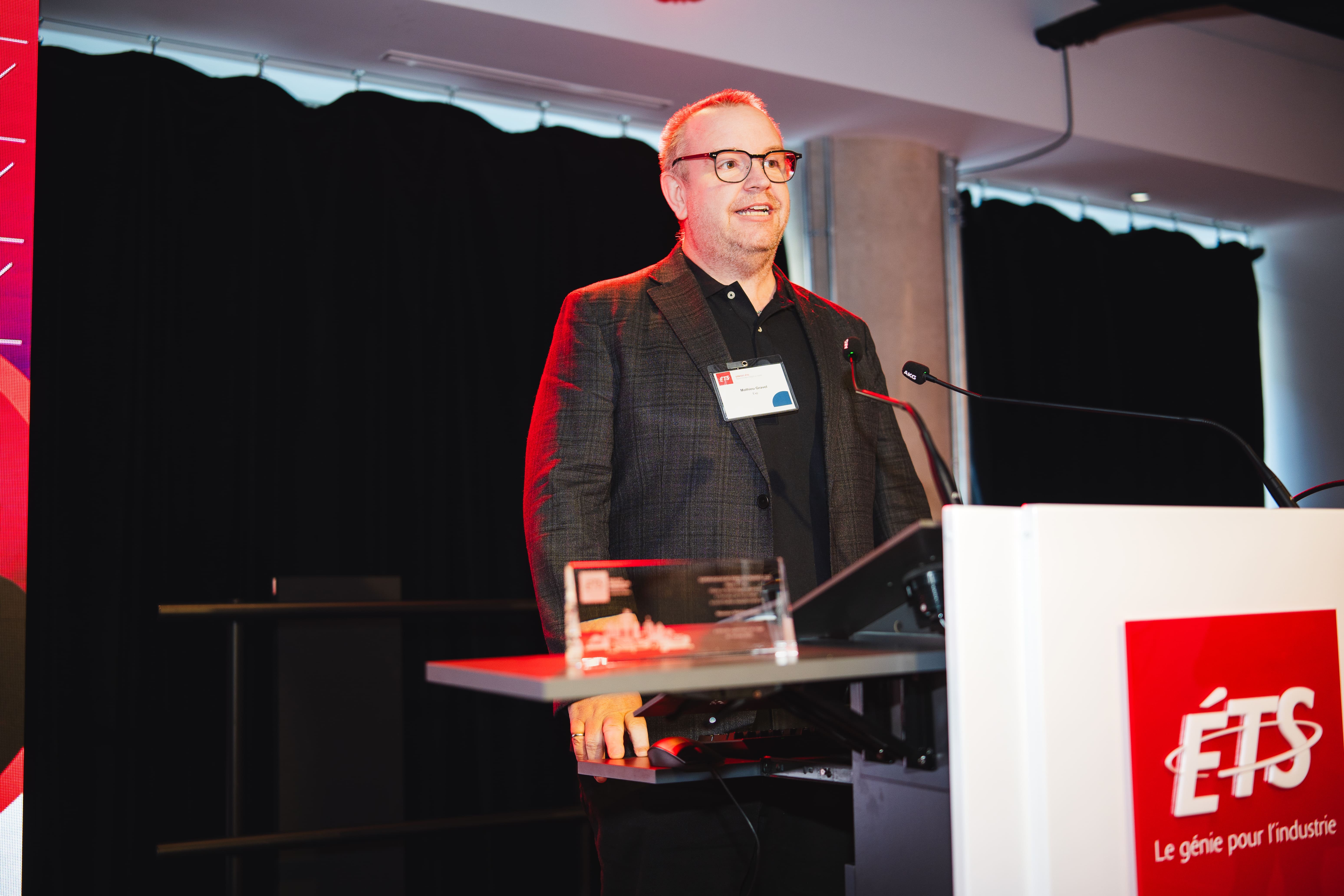 Un conférencier s'exprime avec enthousiasme devant un public, soulignant l'importance de l'innovation en technologie.