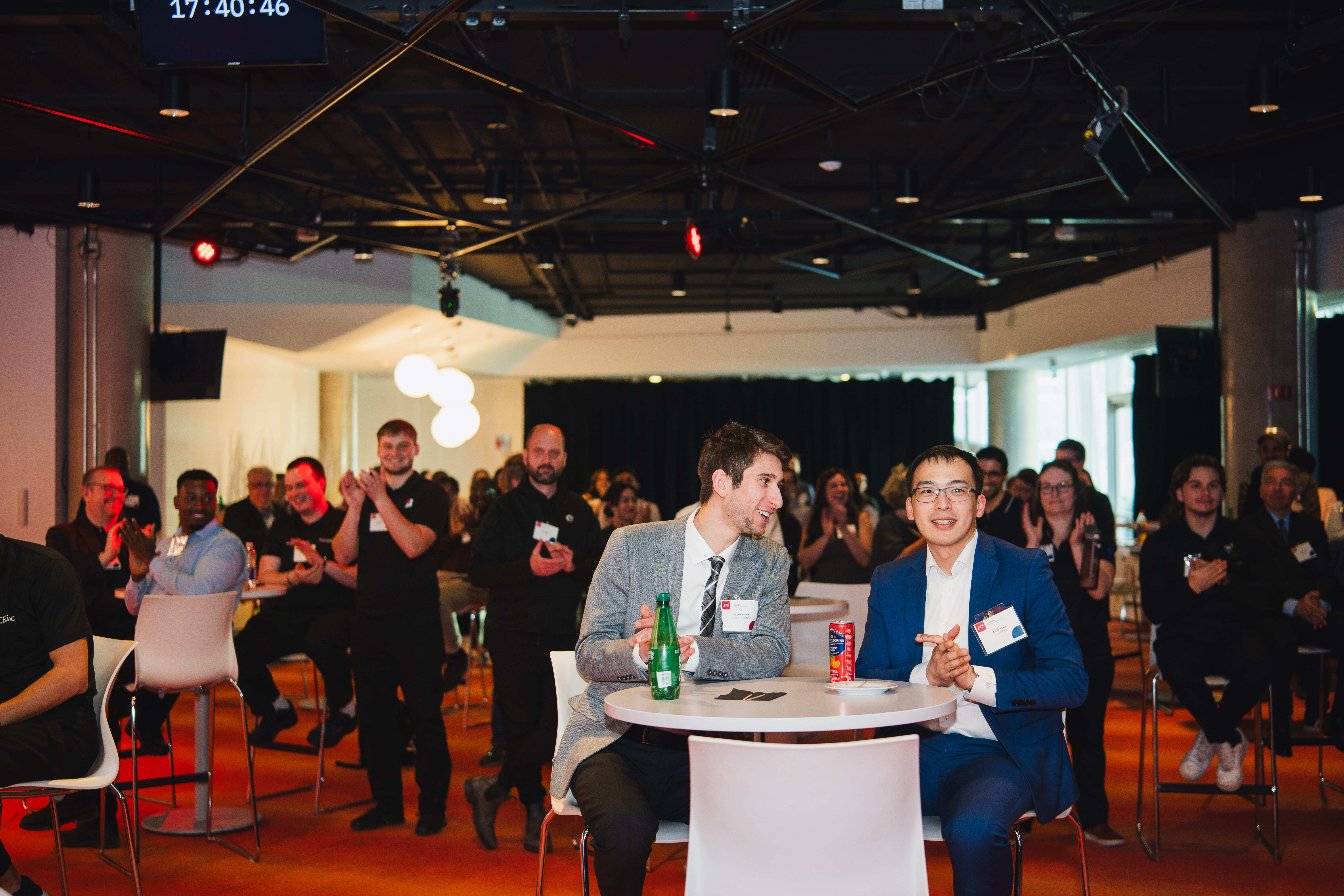 Événement dynamique avec des participants applaudissant, créant une ambiance de partage et d'enthousiasme au sein d'un espace moderne.