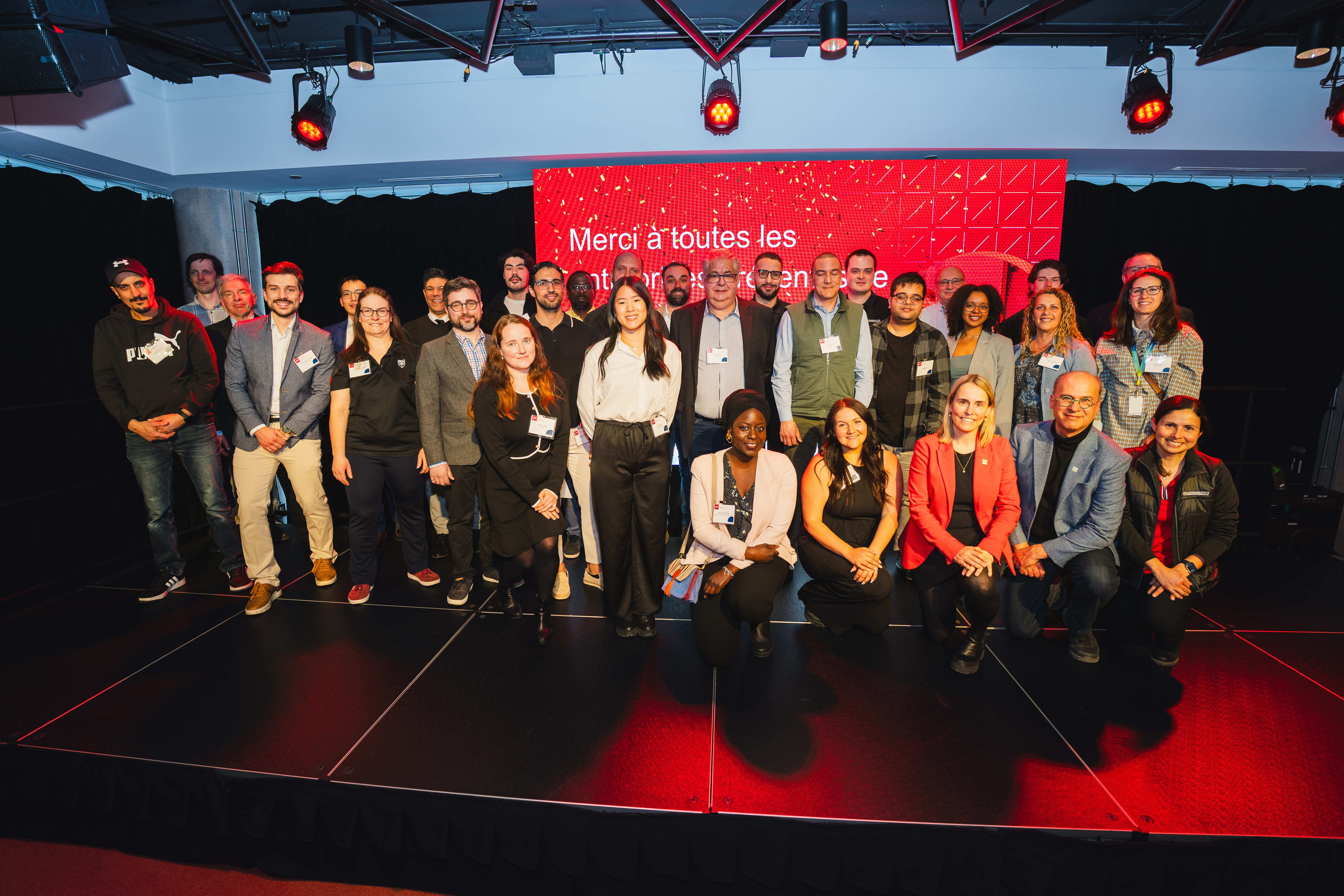 Un groupe de participants pose sur scène, remerciant tous les contributeurs d'un événement académique. Ambiance festive et conviviale.