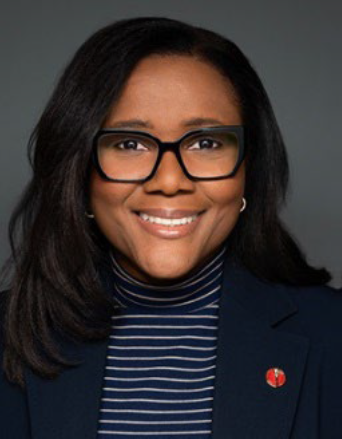 Portrait d'une femme souriante portant des lunettes, un blazer sombre et un pull à rayures, affichant une attitude professionnelle et engageante.