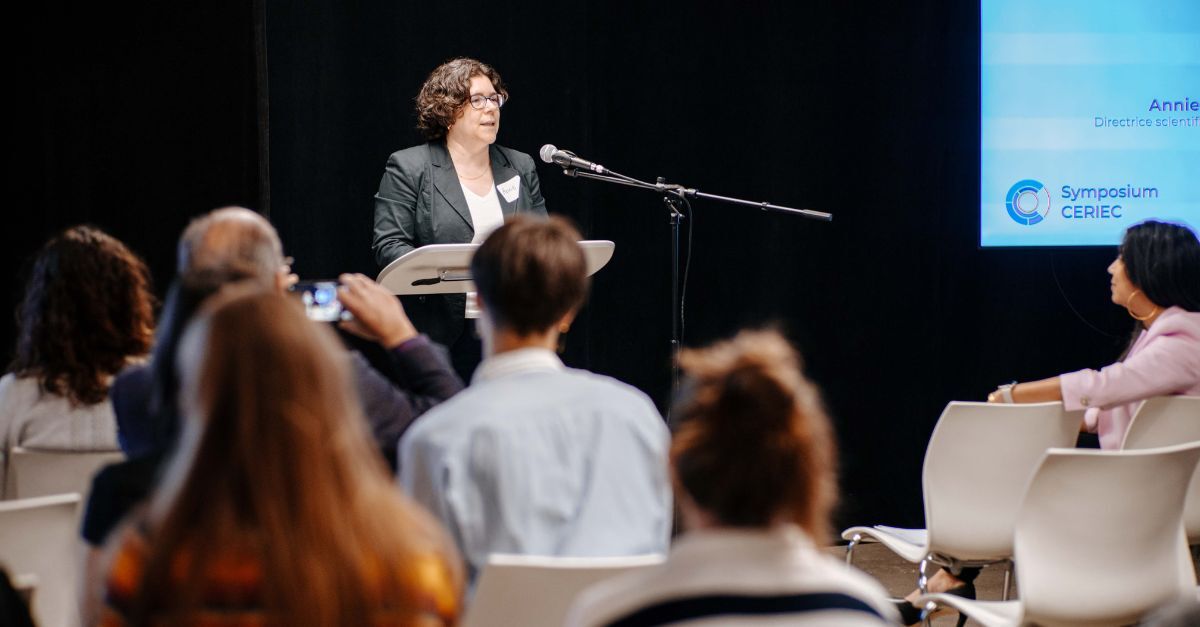 Une intervenante présente un discours lors d'un symposium, captivant l'attention d'un public attentif.