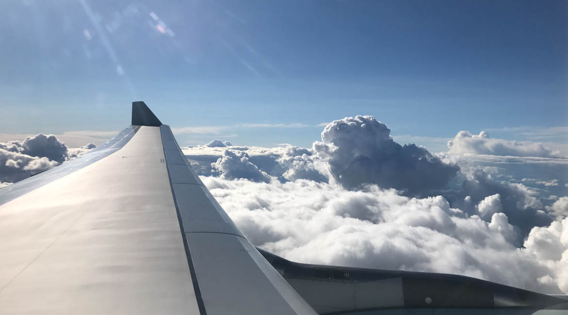 Vue aérienne depuis un avion, aile sur nuages cotonneux et ciel bleu.