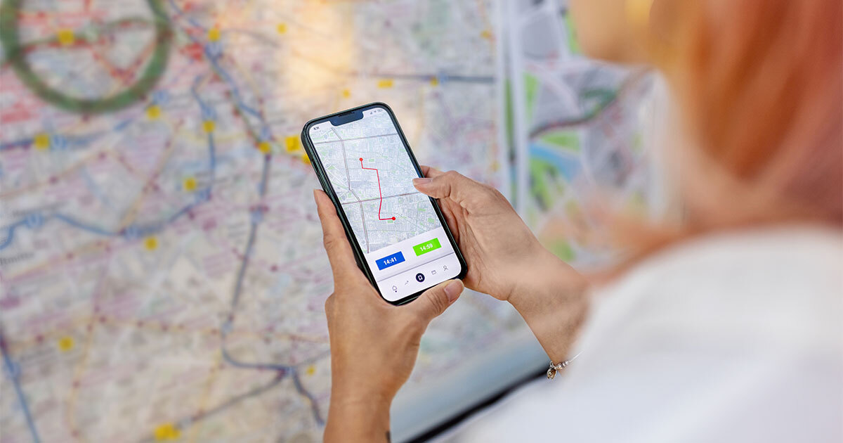 A person uses a smartphone to navigate a route, with a detailed map visible in the background.