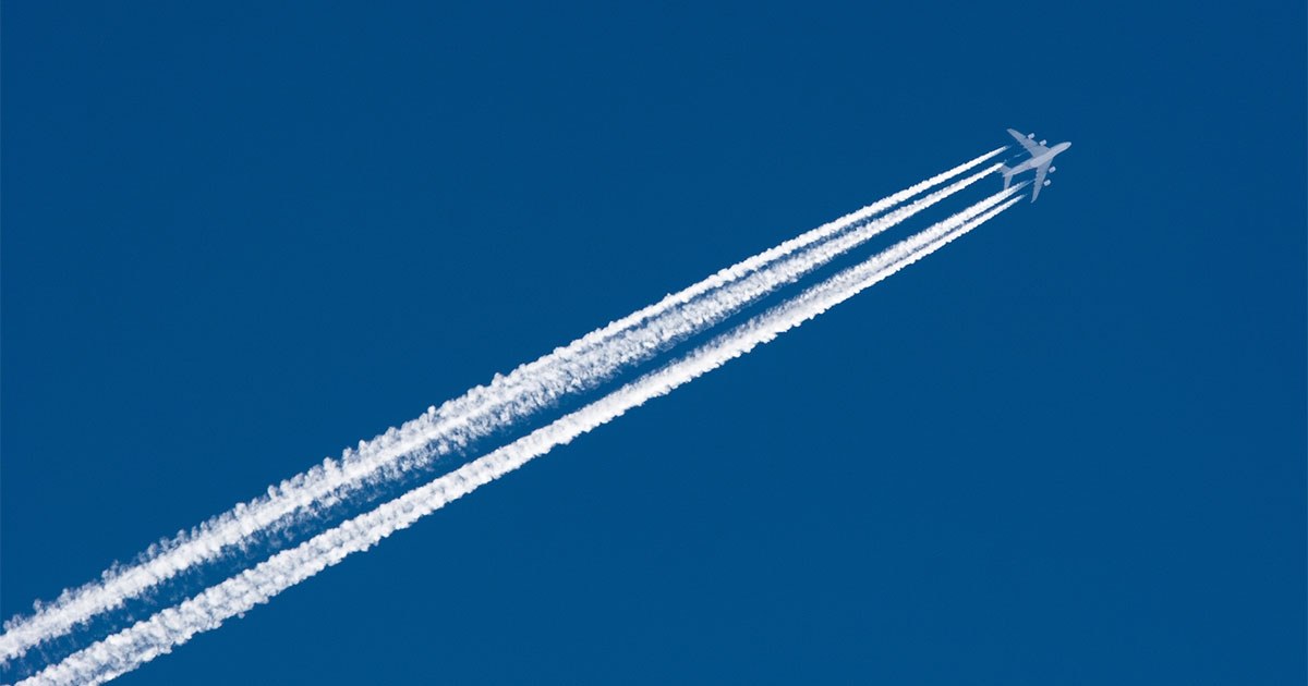 Un avion traverse un ciel dégagé, laissant derrière lui des traînées de condensation blanches dans un bleu éclatant.
