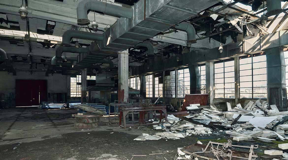 Salle industrielle délabrée avec débris et installations suspendues.