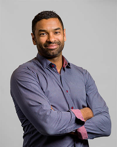 Un professeur souriant, vêtu d'une chemise à motifs, présente un air confiant et accessible, incarnant le dynamisme de l'enseignement supérieur.