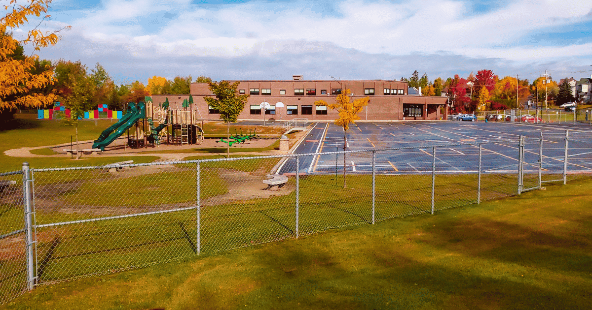 Un parc scolaire avec des jeux, des arbres colorés et une cour spacieuse entourée d'une clôture, reflétant un environnement éducatif agréable.