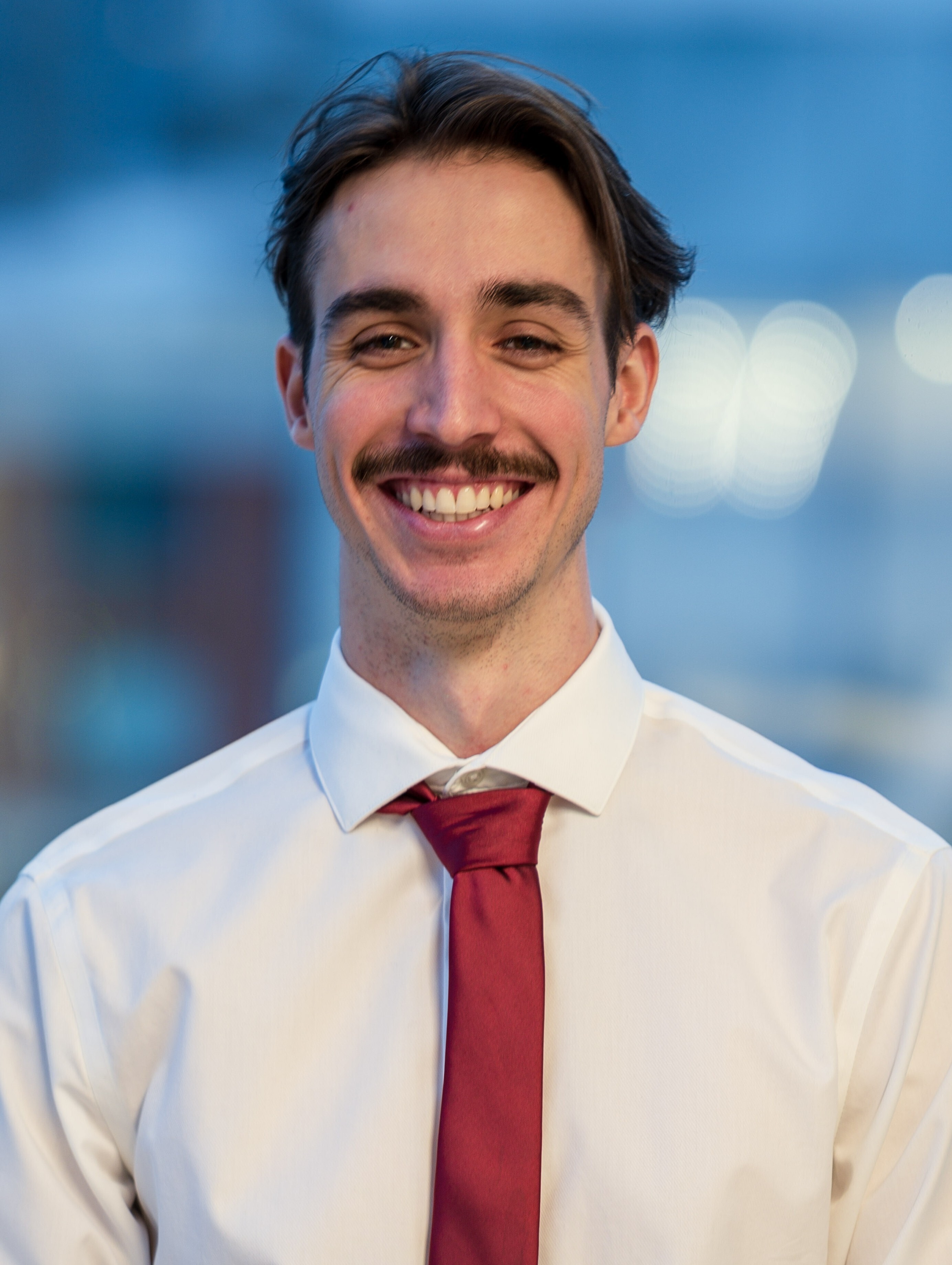 Un étudiant souriant en chemise blanche et cravate rouge, prêt à relever de nouveaux défis académiques dans une ambiance dynamique.