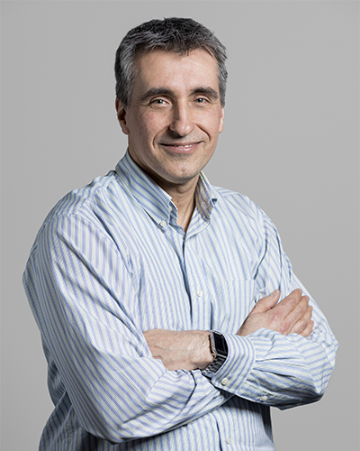 Portrait d'un homme souriant avec les bras croisés, vêtu d'une chemise à rayures, dégageant une image amicale et professionnelle.